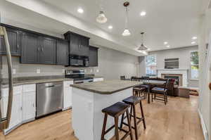 Kitchen with white cabinets, hanging light fixtures, a breakfast bar area, light hardwood, and stainless steel appliances