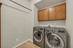 Laundry area with washer and dryer, light wood flooring, and cabinets