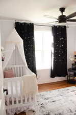 Bedroom featuring ceiling fan, wood-type flooring, and a crib