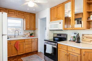 Kitchen featuring dark parquet floors, ceiling fan, sink, and white appliances