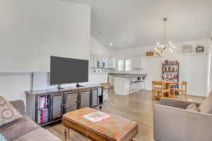 Living room featuring sink, a notable chandelier, high vaulted ceiling, and light wood-type flooring