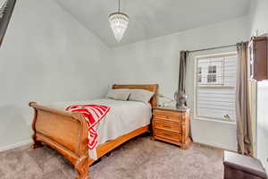 Bedroom with an inviting chandelier, lofted ceiling, and carpet