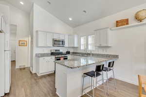 Kitchen featuring kitchen peninsula, stainless steel appliances, light wood-type flooring, white cabinets, and light stone counters