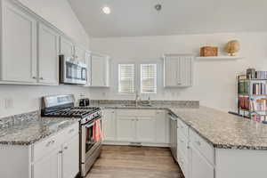 Kitchen featuring sink, white cabinetry, stainless steel appliances, lofted ceiling, and light hardwood / wood-style flooring