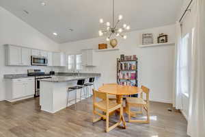 Dining space with sink, light hardwood / wood-style floors, vaulted ceiling, and an inviting chandelier