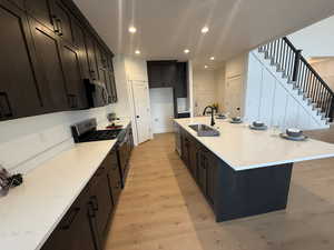 Kitchen featuring appliances with stainless steel finishes, light stone counters, sink, a center island with sink, and light hardwood / wood-style flooring