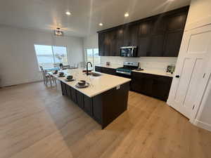 Kitchen featuring appliances with stainless steel finishes, light wood-type flooring, an island with sink, and sink