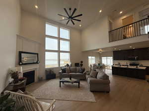 Living room with ceiling fan, plenty of natural light, light hardwood / wood-style floors, and a high ceiling