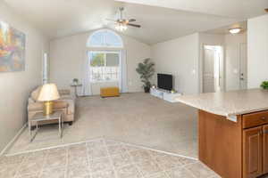 Carpeted living room with lofted ceiling and ceiling fan