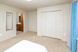 Bedroom with a closet, ensuite bathroom, and light colored carpet