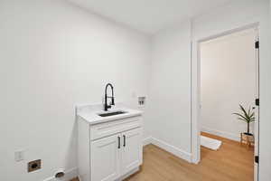 Laundry area featuring electric dryer hookup, washer hookup, sink, cabinets, and light hardwood / wood-style floors