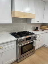 Kitchen featuring light hardwood / wood-style floors, light stone counters, high end range, white cabinets, and backsplash