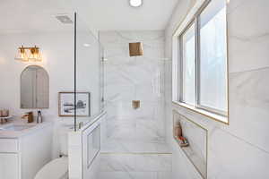 Bathroom with vanity, toilet, a healthy amount of sunlight, and tiled shower