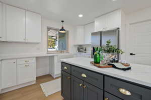 Kitchen with sink, stainless steel fridge with ice dispenser, decorative light fixtures, white cabinetry, and light hardwood / wood-style floors