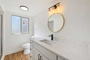 Bathroom with toilet, walk in shower, vanity, and wood-type flooring