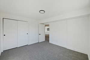 Unfurnished bedroom featuring a closet and dark colored carpet