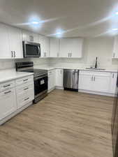 Kitchen with light wood-type flooring, appliances with stainless steel finishes, sink, and white cabinets