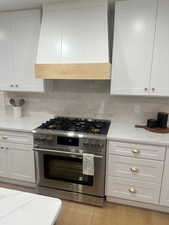 Kitchen featuring white cabinets, stainless steel stove, light stone counters, and tasteful backsplash