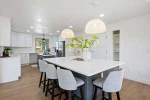 Kitchen featuring a center island, hanging light fixtures, stainless steel fridge with ice dispenser, white cabinets, and light hardwood / wood-style flooring