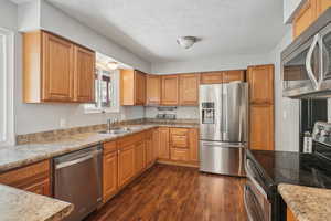 Kitchen with dark hardwood / wood-style flooring, appliances with stainless steel finishes, a textured ceiling, light stone countertops, and sink