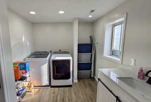 Washroom featuring washer and dryer, a textured ceiling, sink, and light hardwood / wood-style floors