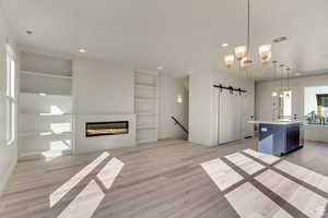 Kitchen with a center island with sink, a barn door, a chandelier, light hardwood / wood-style flooring, and pendant lighting