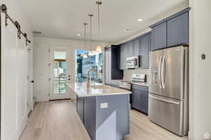 Kitchen featuring a kitchen island with sink, light hardwood / wood-style flooring, hanging light fixtures, stainless steel appliances, and a barn door