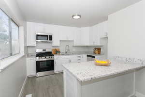 Kitchen featuring light stone counters, white cabinetry, light wood-type flooring, sink, and stainless steel appliances