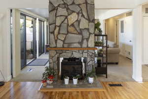 Living room with a stone fireplace, electric panel, and hardwood / wood-style floors