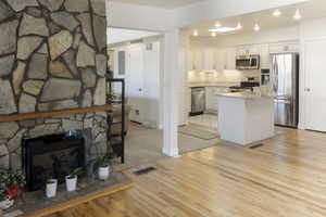 Kitchen with white cabinets, appliances with stainless steel finishes, light wood-type flooring, a stone fireplace, and a center island