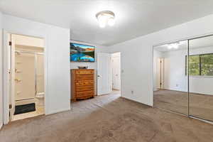 Unfurnished bedroom with a closet, light carpet, a textured ceiling, and ensuite bathroom