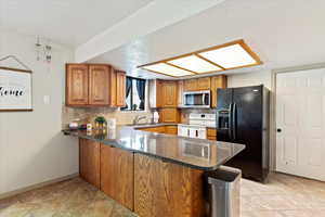 Kitchen featuring kitchen peninsula, electric range, backsplash, and black fridge with ice dispenser