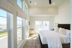 Carpeted bedroom featuring multiple windows, a high ceiling, and ceiling fan