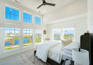 Carpeted bedroom featuring a water view, ceiling fan, a towering ceiling, and multiple windows