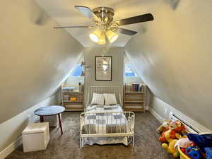 Bedroom featuring baseboard heating, ceiling fan, lofted ceiling, and dark colored carpet