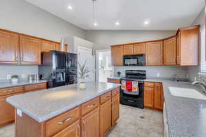 Kitchen featuring lofted ceiling, sink, black appliances, a center island, and light tile patterned floors