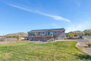 Back of house featuring a deck with mountain view, a patio area, a lawn, and solar panels