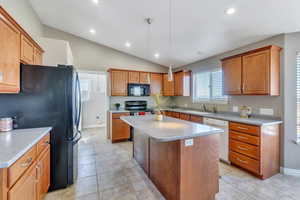 Kitchen featuring lofted ceiling, black appliances, pendant lighting, and a kitchen island