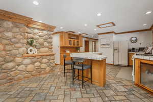 Kitchen featuring white fridge with ice dispenser, ornamental molding, tile counters, and a center island