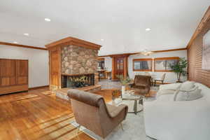 Living room featuring a stone fireplace, brick wall, ornamental molding, ceiling fan, and light hardwood / wood-style flooring