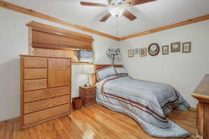 Bedroom with ceiling fan, light hardwood / wood-style floors, and crown molding