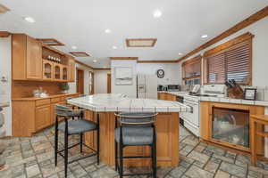 Kitchen featuring white appliances, crown molding, a kitchen island, and tile counters