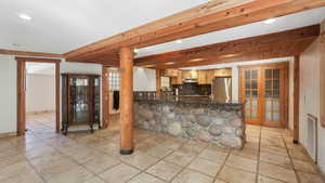 Kitchen featuring light brown cabinetry, backsplash, kitchen peninsula, beam ceiling, and stainless steel refrigerator