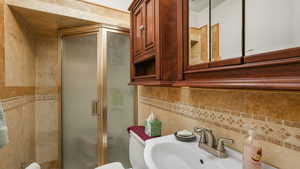 Half bathroom ensuite featuring sink, a shower with shower door, toilet, tile walls, and decorative backsplash