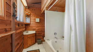 Full bathroom with toilet, wood walls, shower / bath combo, jetted tub, vanity, and tile patterned floors