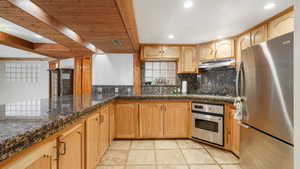 Kitchen featuring wood ceiling, decorative backsplash, appliances with stainless steel finishes, dark marble counters, and sink