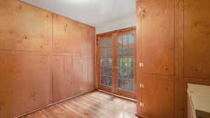 Storage room featuring french doors, light hardwood / wood-style flooring, and wooden cabinets