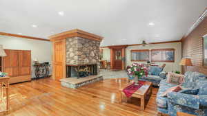 Living room with ornamental molding, hardwood floors, a fireplace, and ceiling fan