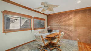 Dining room with ceiling fan, brick wall, and ornamental molding