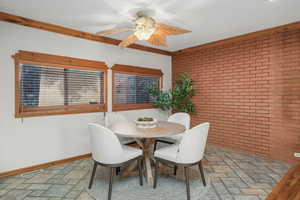 Dining room with ornamental molding, ceiling fan, and brick wall